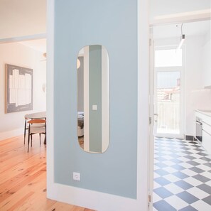 A room with a light blue wall, a wooden floor, a dining area with a table and chairs, and a kitchen with a checkered floor. - Liiiving in Porto - Art Design Apartment II (Porto)