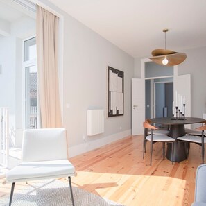 A modern dining area with a round table, white chairs, and a pendant light. - Liiiving in Porto - Art Design Apartment II (Porto)