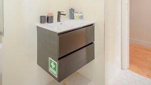 A modern bathroom with a white sink, a round mirror, and a green emergency exit sign. - Liiiving in Porto Historic Cl Rigos Studio - 4F (Porto)