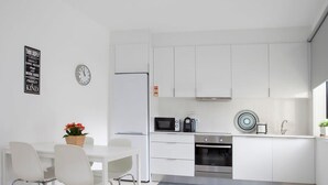 A modern kitchen with white cabinets, a microwave, oven, and a sink. There is a dining area with a table and chairs. - Liiiving in Porto Santa Catarina Cosy Apartment (Porto)