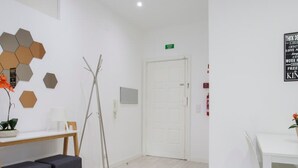 A room with a white door, a table with two chairs, a bench, a hexagonal wall decoration, and a sign above the door. - Liiiving in Porto Santa Catarina Cosy Apartment (Porto)