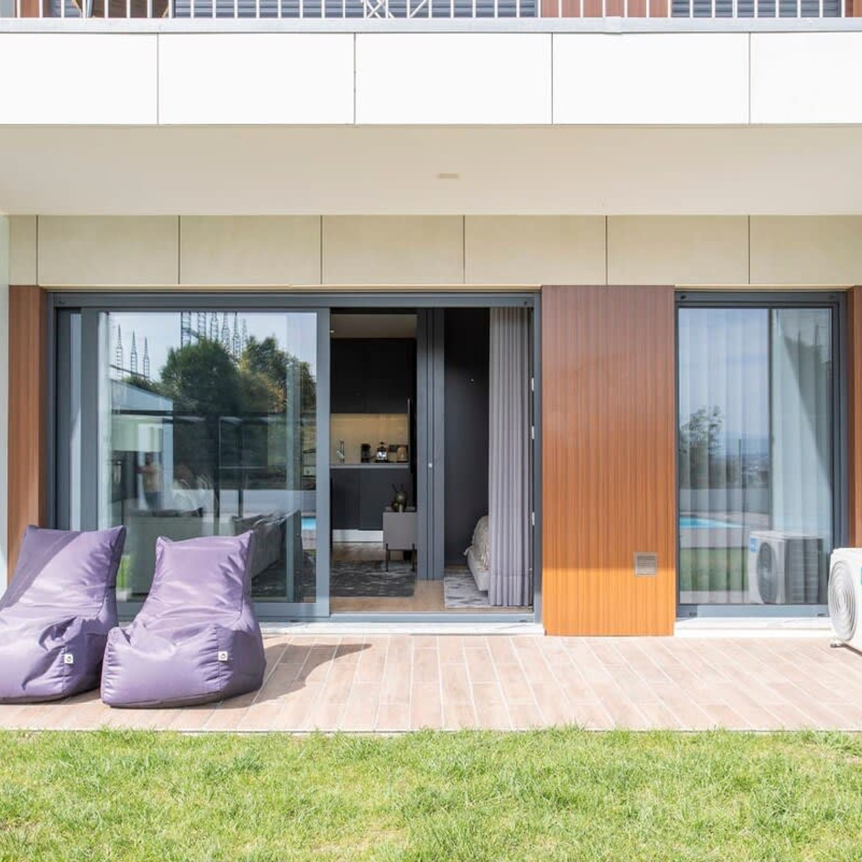 A modern building with a glass entrance, a patio with cushions, and a visible kitchen area.