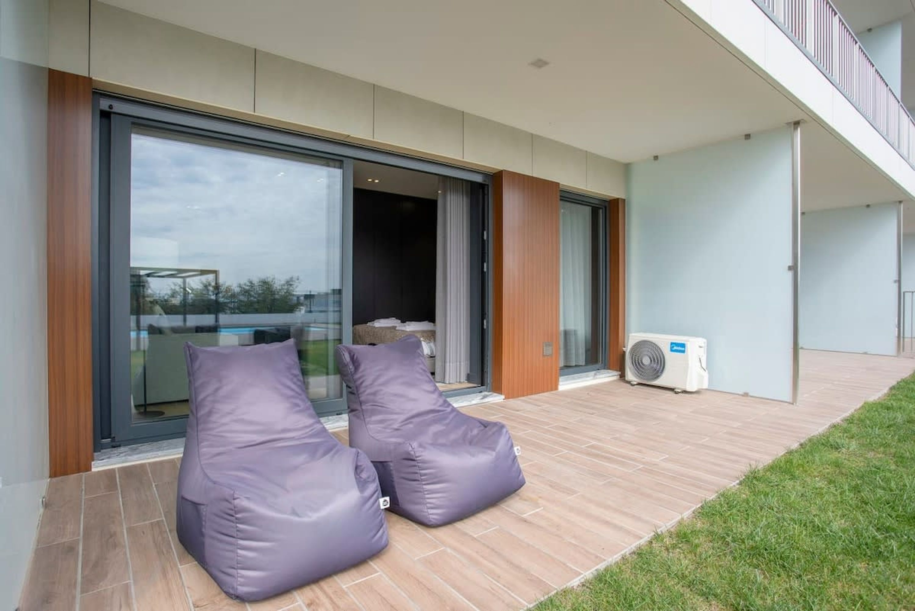 Een moderne buitenruimte met twee loungestoelen, een glazen toegangsdeur en een plafondventilator.