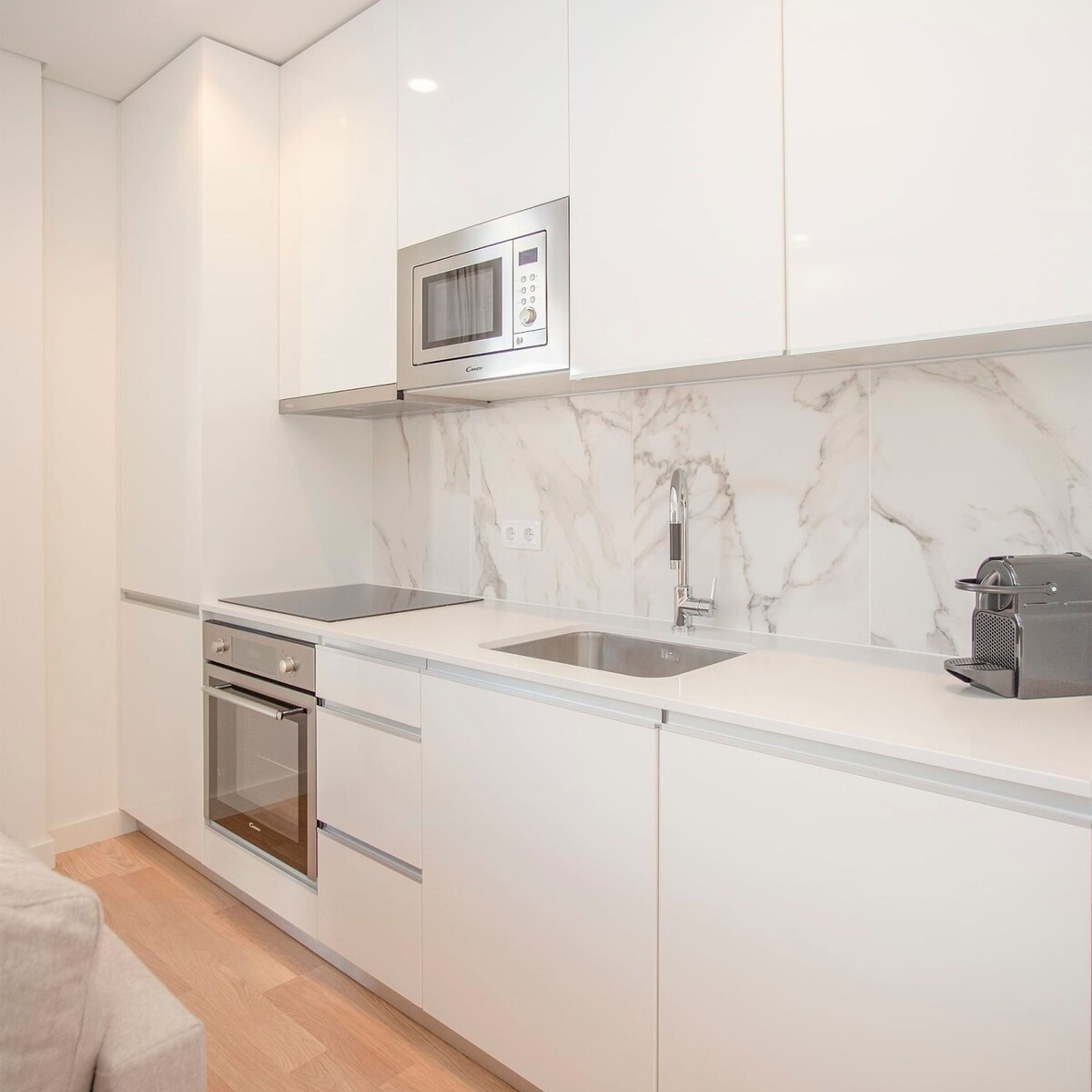 A modern kitchen with white cabinets, a built-in microwave, a stainless steel sink, and a coffee machine.