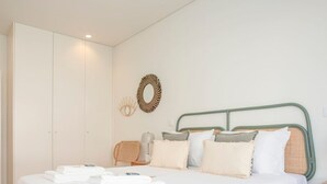 Un lit bien fait, avec du linge de lit blanc et des oreillers, une table de chevet avec une lampe et un miroir fixé au mur.