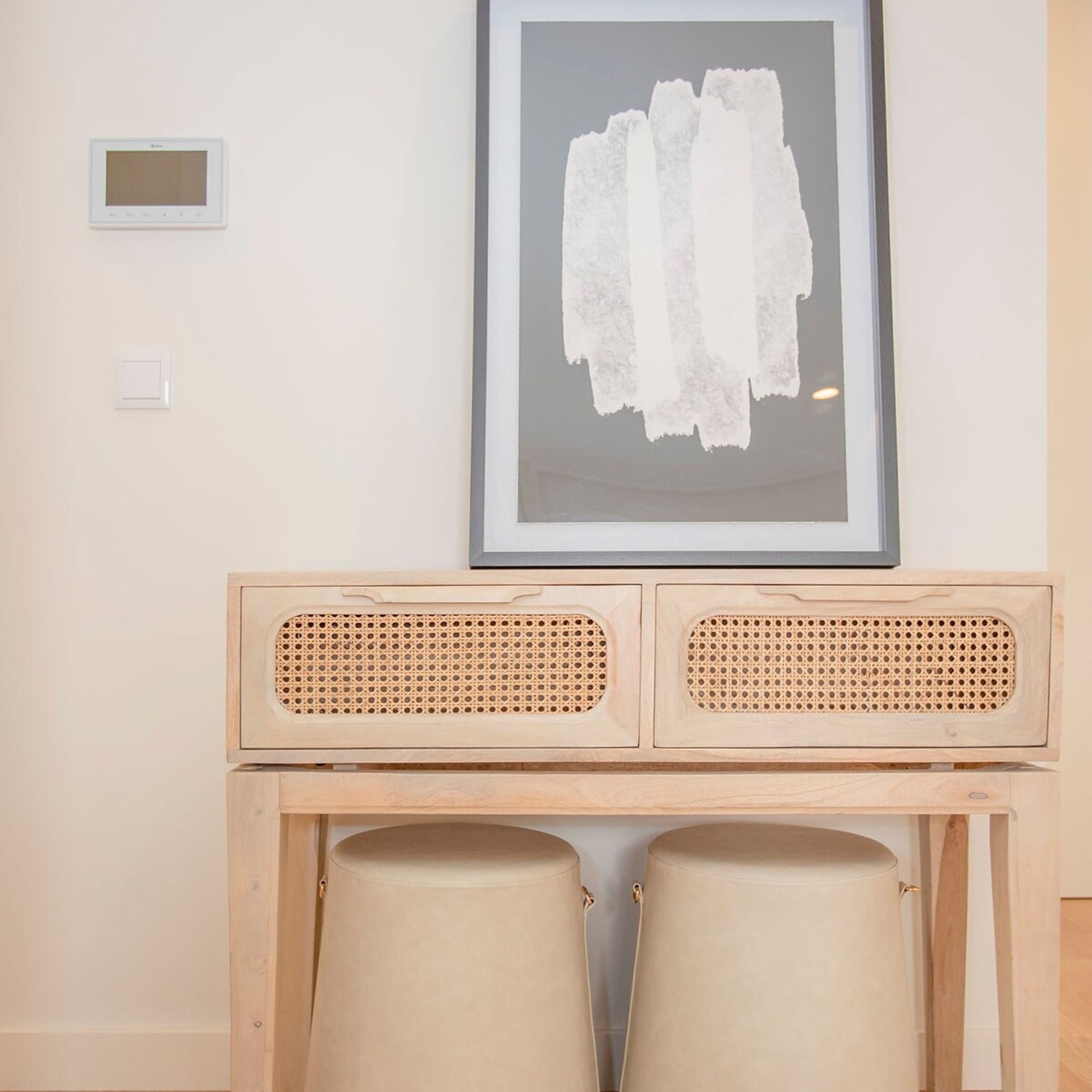 A room with a framed abstract painting, a small control panel, and a wooden desk with two cushioned chairs.