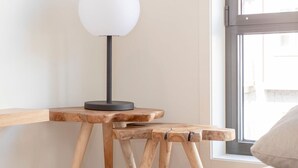 Une pièce avec une table en bois, une lampe, une fenêtre et un lit avec un oreiller.