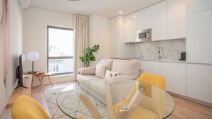 Un appartement moderne comprenant un espace de vie, une table à manger en verre, un canapé et une cuisine avec des meubles blancs et un dosseret en marbre.