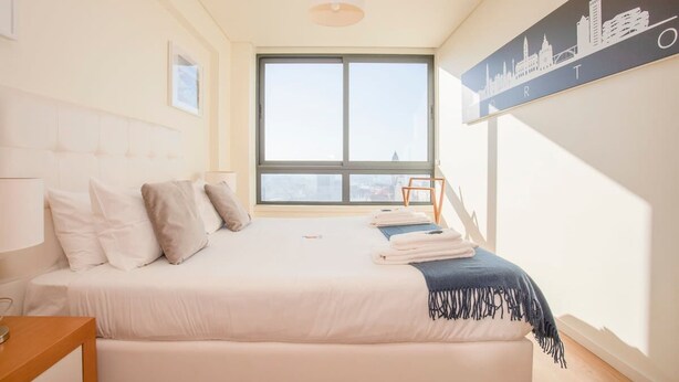 A hotel bedroom with a large bed, a city skyline artwork on the wall, and a window with a view of buildings. - Liiiving in Porto Downtown View Apartment (Porto)