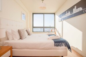 A hotel bedroom with a large bed, a city skyline artwork on the wall, and a window with a view of buildings. - Liiiving in Porto Downtown View Apartment (Porto)