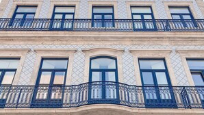 Un edificio a più piani con facciata in tegole, balconi con ringhiere in ferro battuto decorate e cielo sereno.