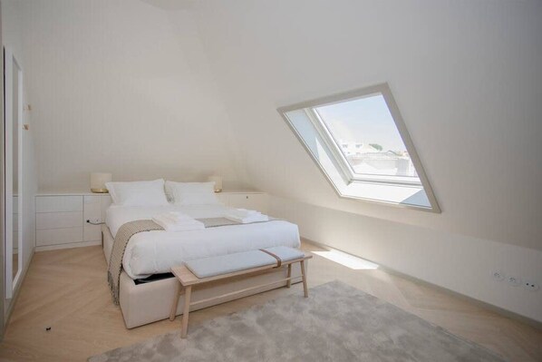 A bedroom with a skylight, a bed, a bedside table, and a bench. - Liiiving in Porto Luxury Beachfront Apartment VI (Porto)