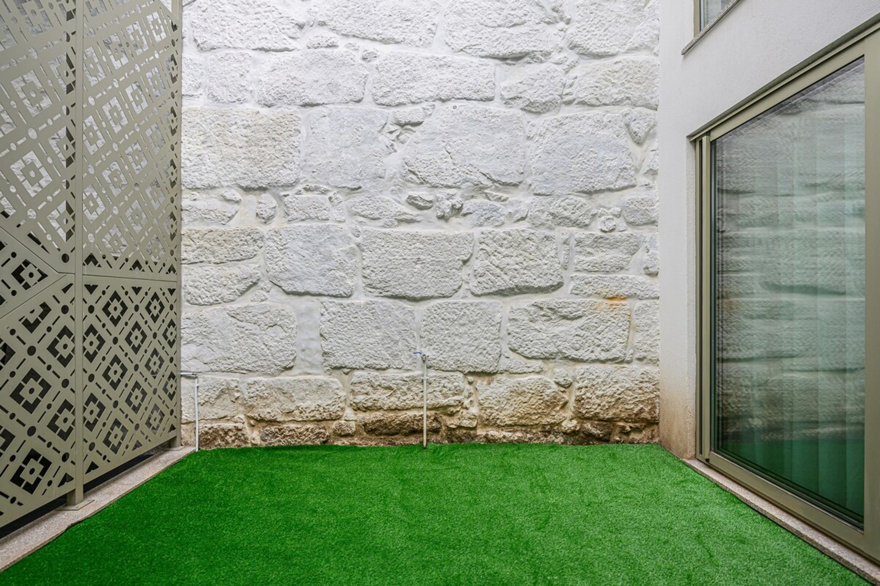 A corner with a white stone wall, green artificial grass, and a white decorative panel.