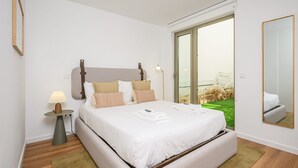 Un dormitorio moderno con una cama grande, una mesita de noche con lámpara y vistas a un paisaje verde a través de una puerta corrediza de vidrio.