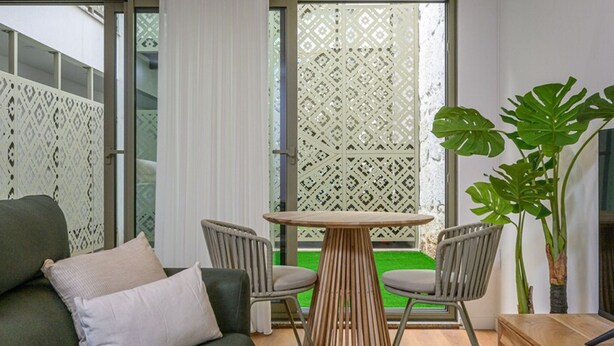 Una sala de estar moderna con un sofá verde, dos sillones, una mesa de madera y una planta grande.