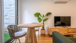 Una sala de estar moderna con una mesa redonda de madera, dos sillas, un sofá verde, una planta en maceta, un televisor y un mueble de madera.