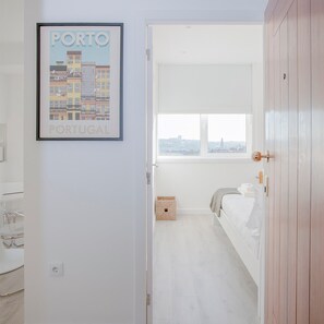 A narrow hallway leading to a bedroom with a bed and a window. A framed picture of Porto, Portugal is on the wall. - Liiiving in Porto Center Spot Apartment (Porto)