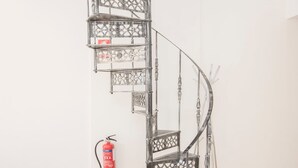 A spiral staircase with a metal railing and a fire extinguisher mounted on the wall. - Liiiving in Porto - Downtown Balcony Apartment (Porto)