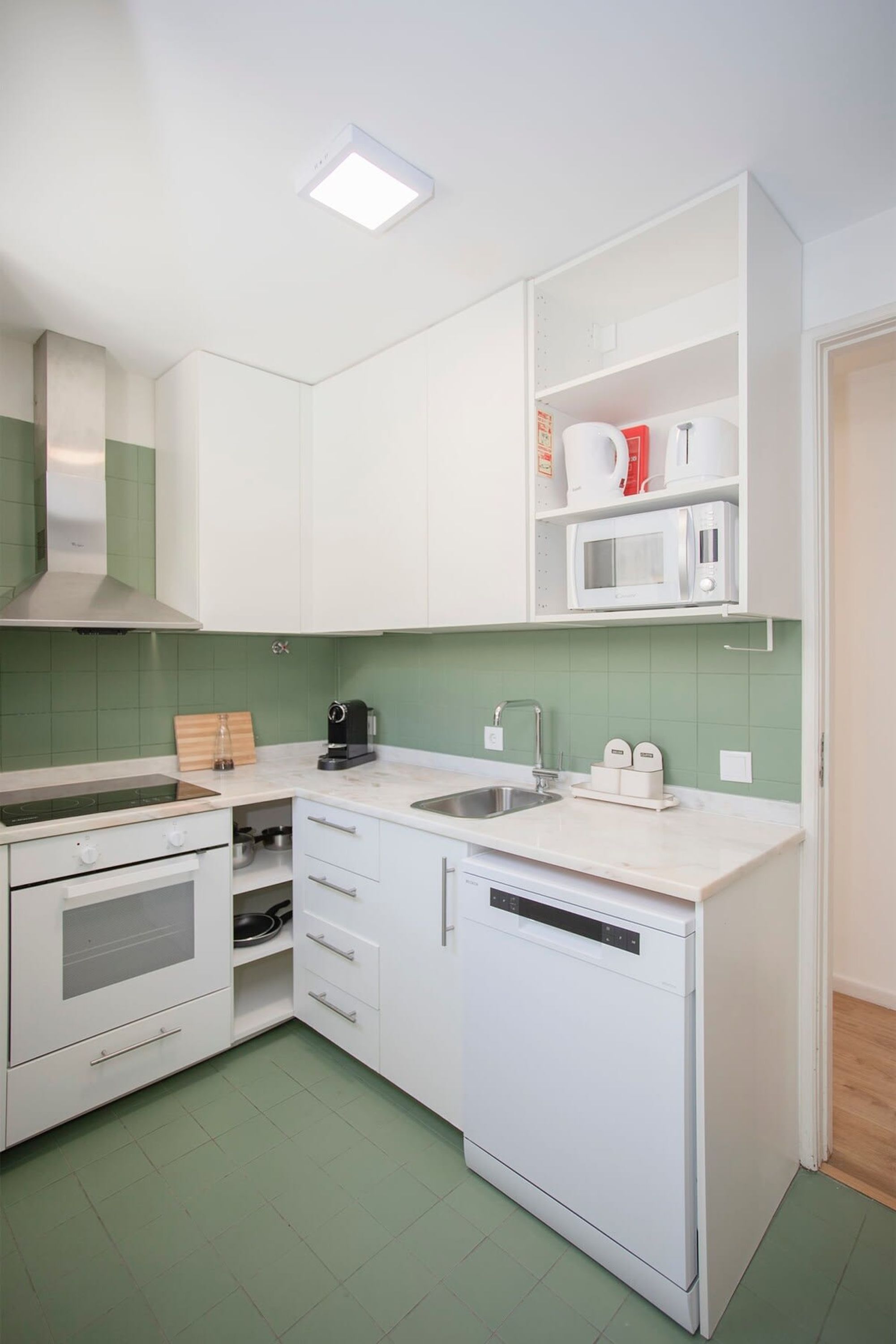A compact kitchen with white cabinets, a microwave, a coffee maker, and a dishwasher.