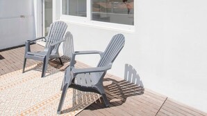 A rooftop terrace with two Adirondack chairs, a patterned rug, and a white wall with a window. - Liiiving in Porto - Downtown Balcony Apartment (Porto)