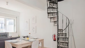 A modern dining area with a spiral staircase, a sofa, and a dining table set for four. - Liiiving in Porto - Downtown Balcony Apartment (Porto)