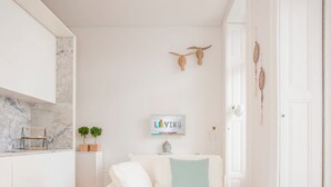 A modern living room with a white sofa, a small table, and a kitchen area with a marble backsplash. - Liiiving in Porto - Downtown Balcony Studio (Porto)