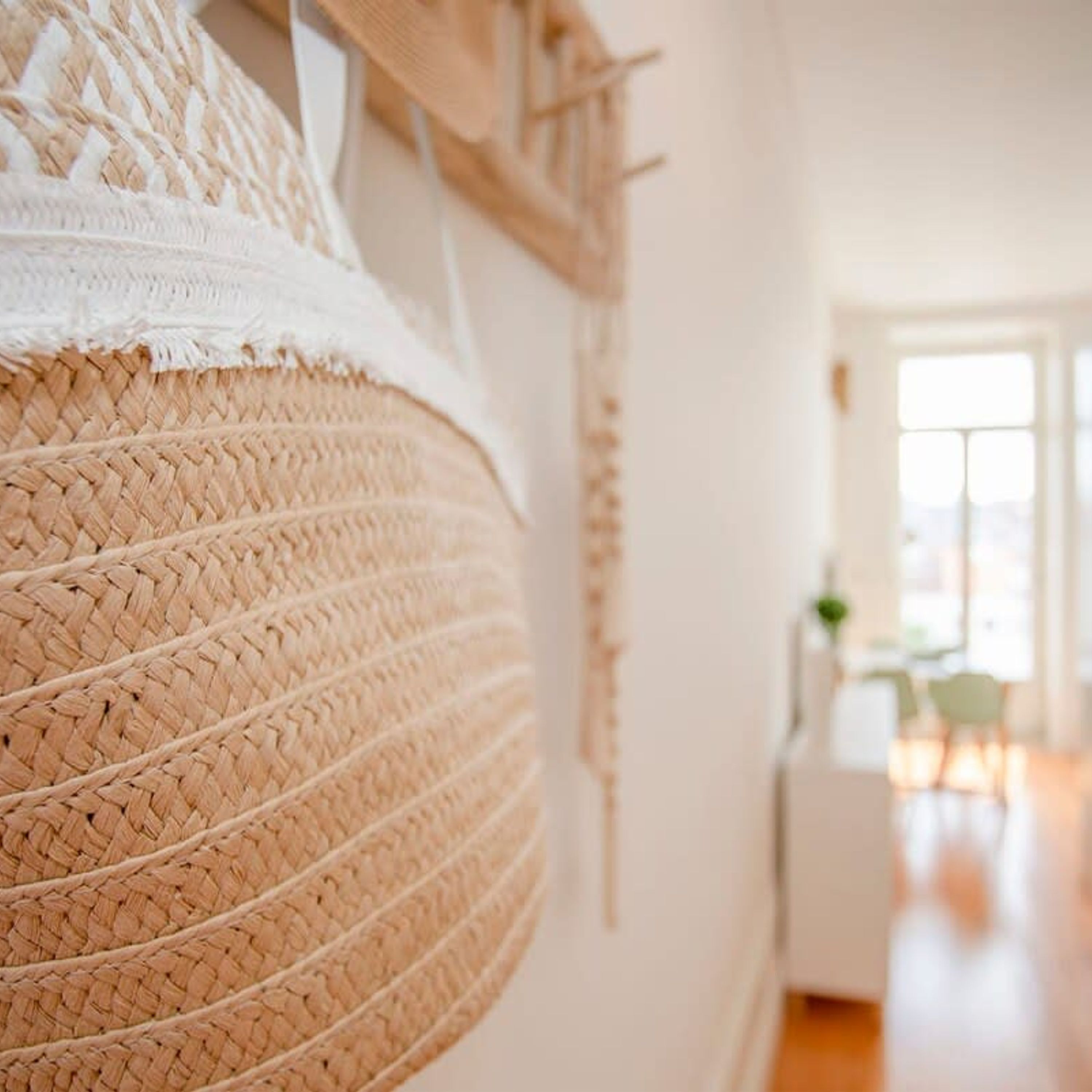 A woven basket hanging on a wall, a white door, and a glimpse of a room with a window and a plant.