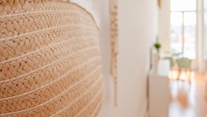 A woven basket hanging on a wall, a white door, and a glimpse of a room with a window and a plant. - Liiiving in Porto - Downtown Balcony Studio (Porto)