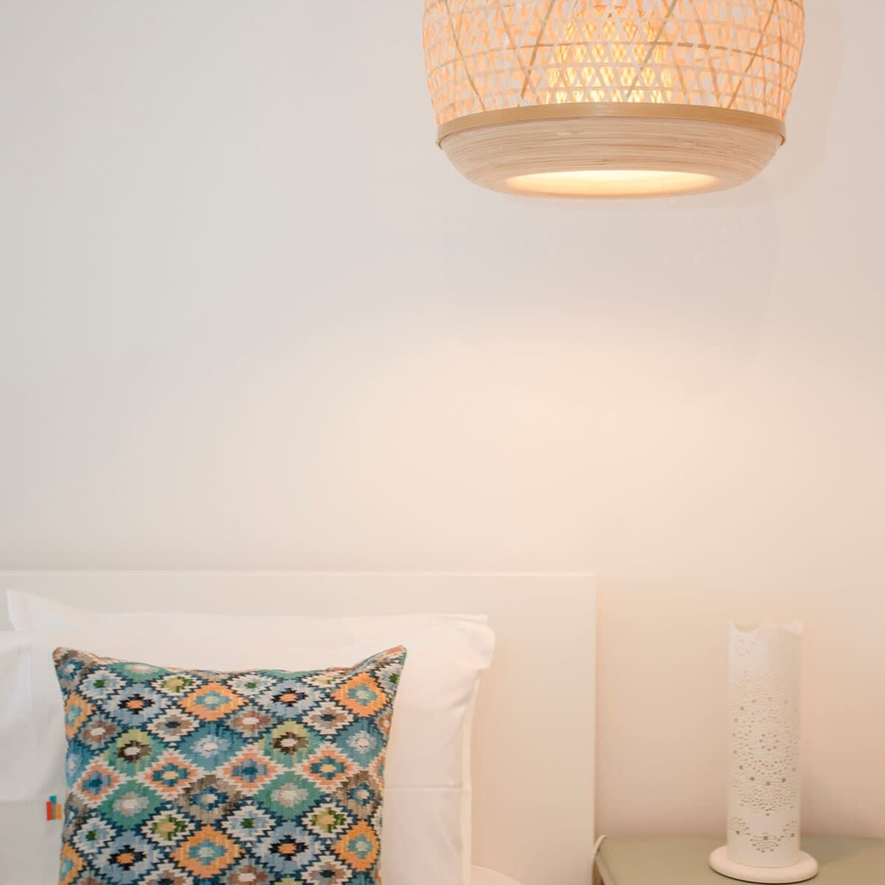 En säng med ett mönstrat kuddöverdrag, en vit vägg och en hängande lampa.