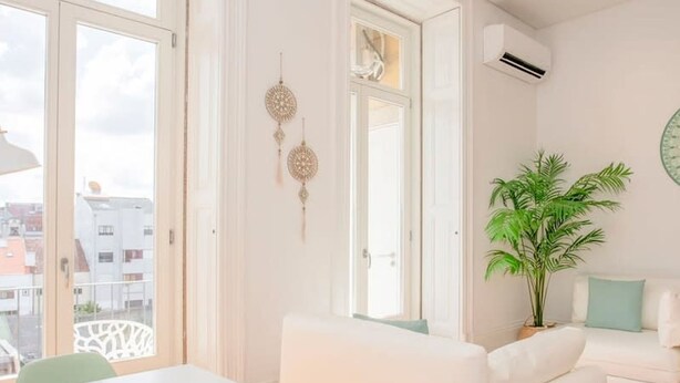 A modern living room with a white sofa, a dining table with chairs, and a potted plant. - Liiiving in Porto - Downtown Balcony Studio (Porto)