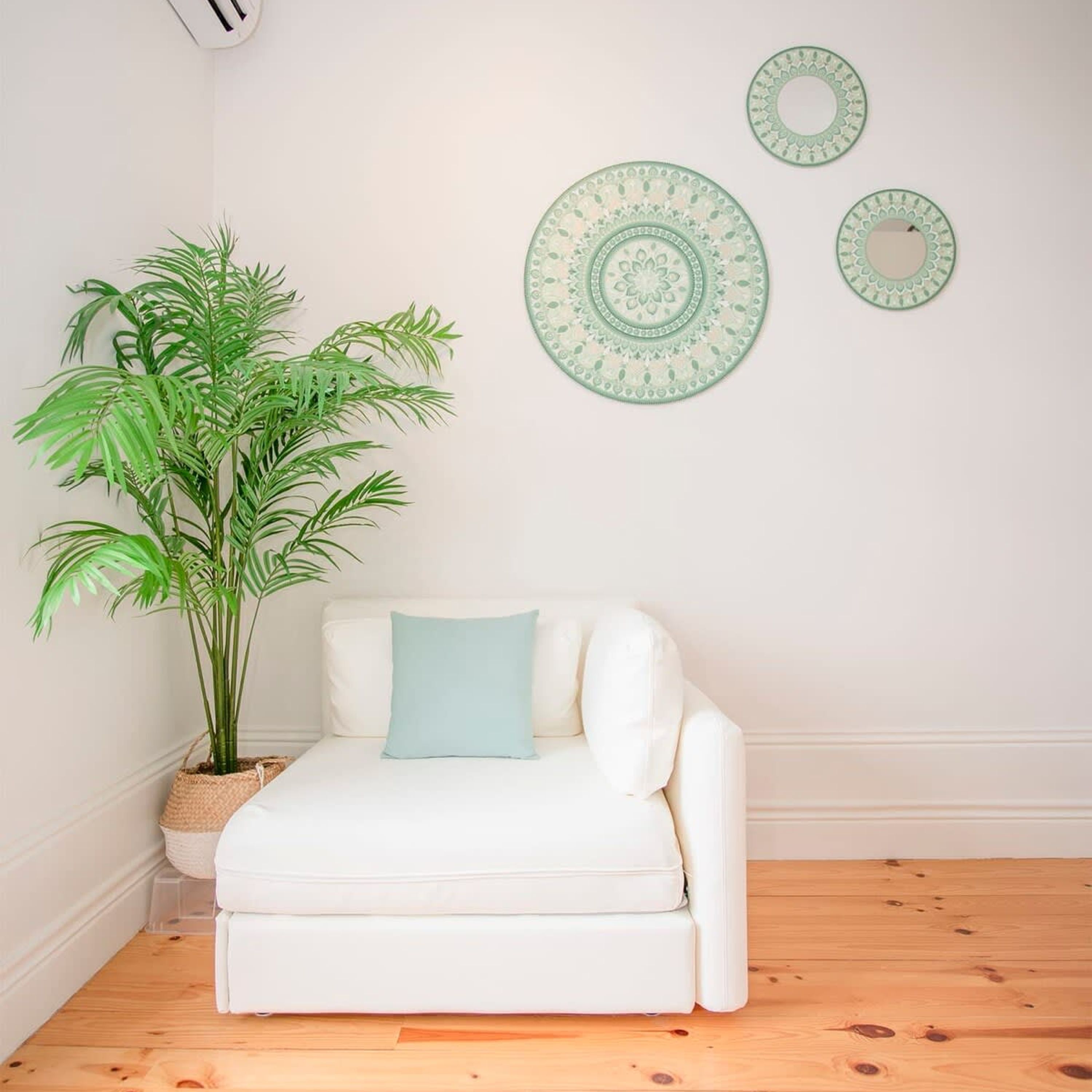 A white sofa with a light blue pillow, a potted plant, and three decorative plates on the wall.