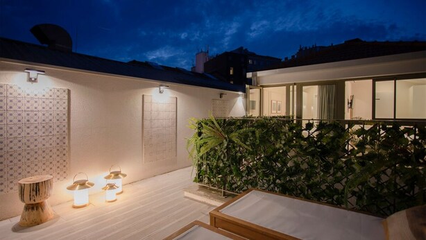 A modern outdoor patio with a wooden deck, a seating area with cushions, and a wall-mounted light fixture. - Liiiving in Porto - Soho Urban Retreat (Porto)