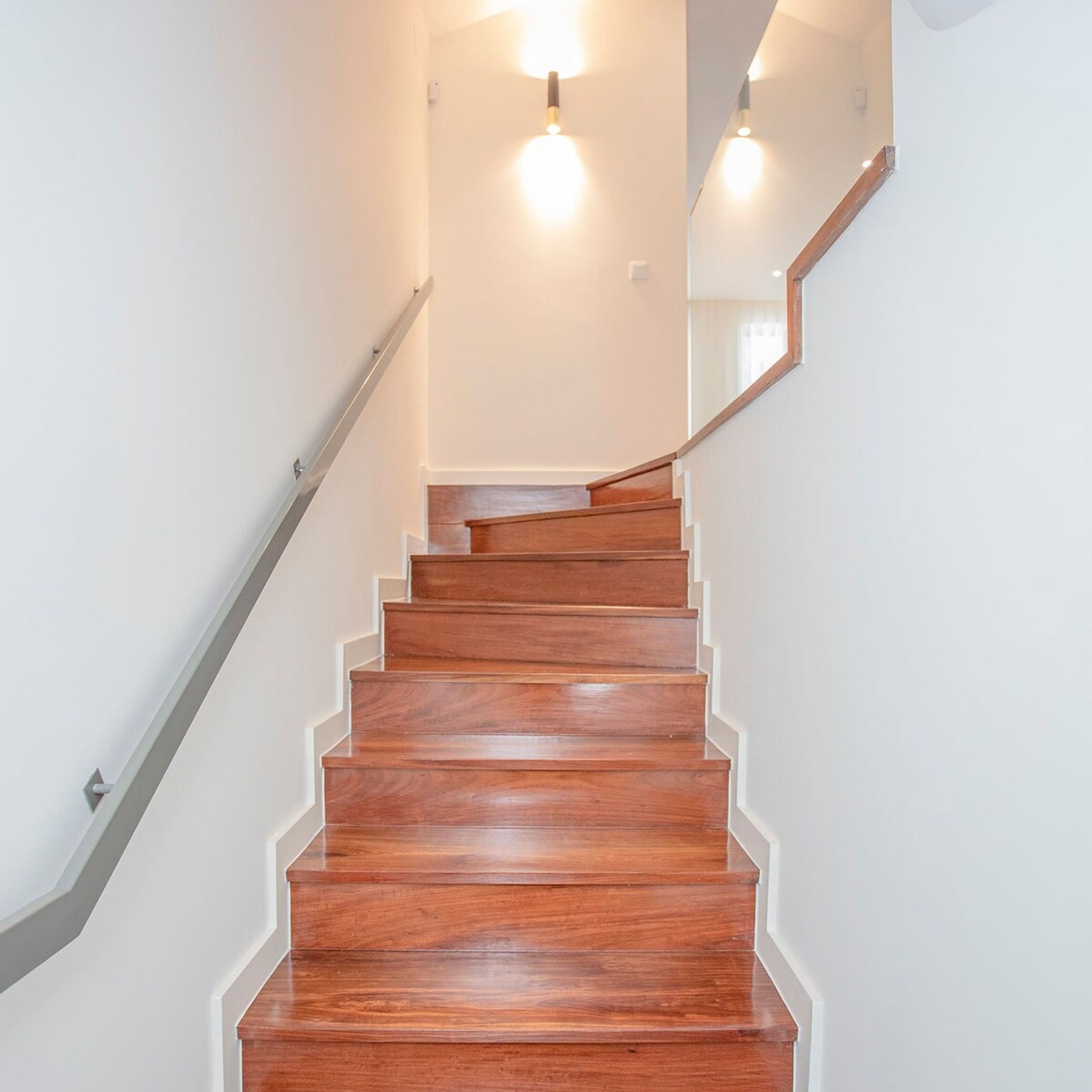 Un escalier en bois, avec des murs blancs et une main courante.