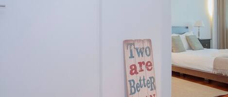 A bedroom with a bed, a bedside table, and a wall-mounted sign that reads "Two are Better Than One".