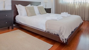 A modern hotel room with a large bed, two bedside tables with lamps, a wooden floor, and a view of the outdoors through sheer curtains. - Liiiving in Porto Balcony Drag o View (Porto)