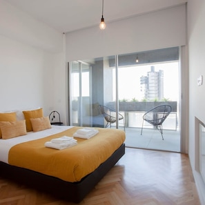 Ein modernes Schlafzimmer mit einem großen Bett, einem Balkon mit Sitzgelegenheiten und Blick auf die Stadt.