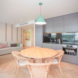 Een moderne keuken met grijze kastjes, een ronde houten tafel, rieten stoelen en een hangende hanglamp.