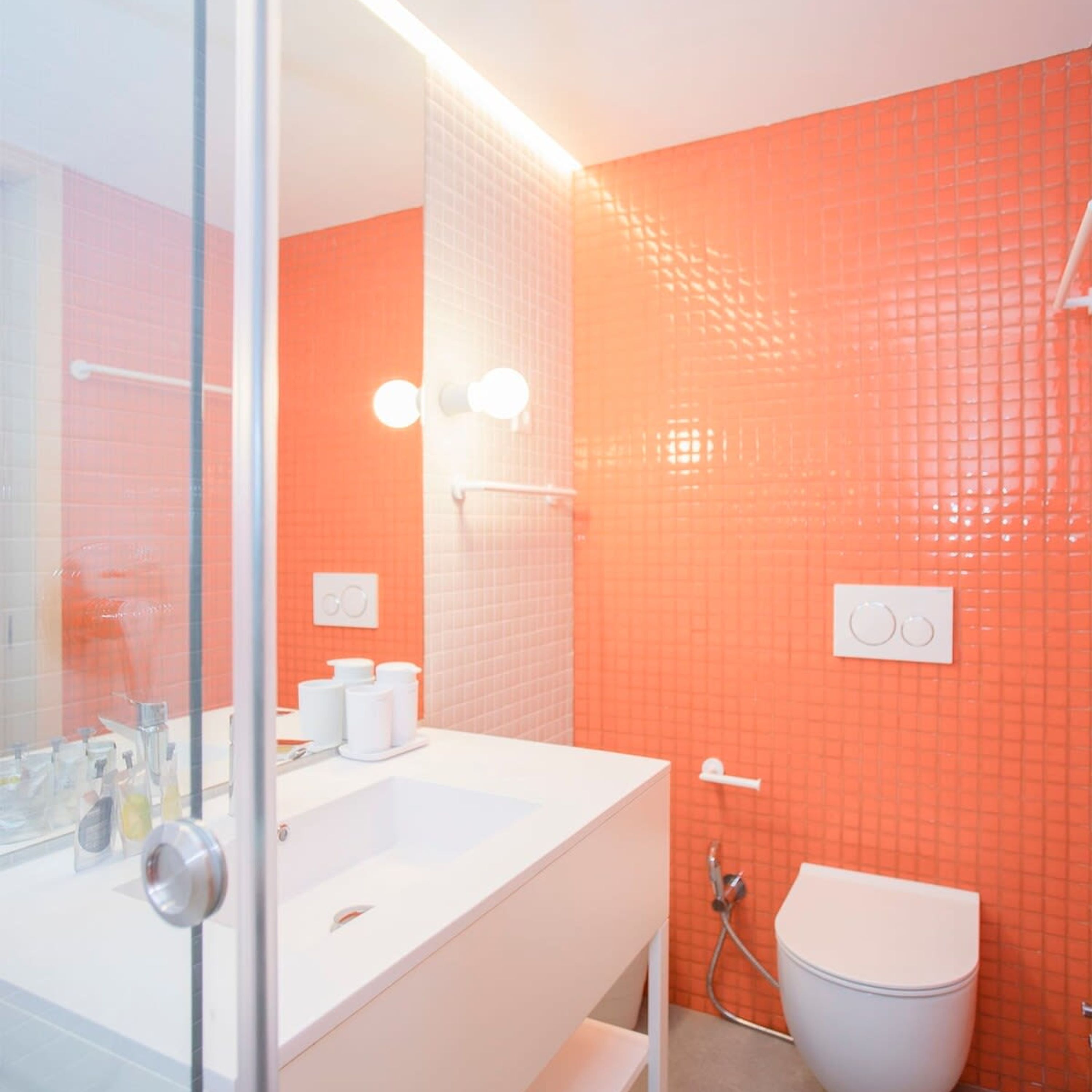 Une salle de bain avec un lavabo blanc, un miroir et des murs recouverts de carreaux orange.