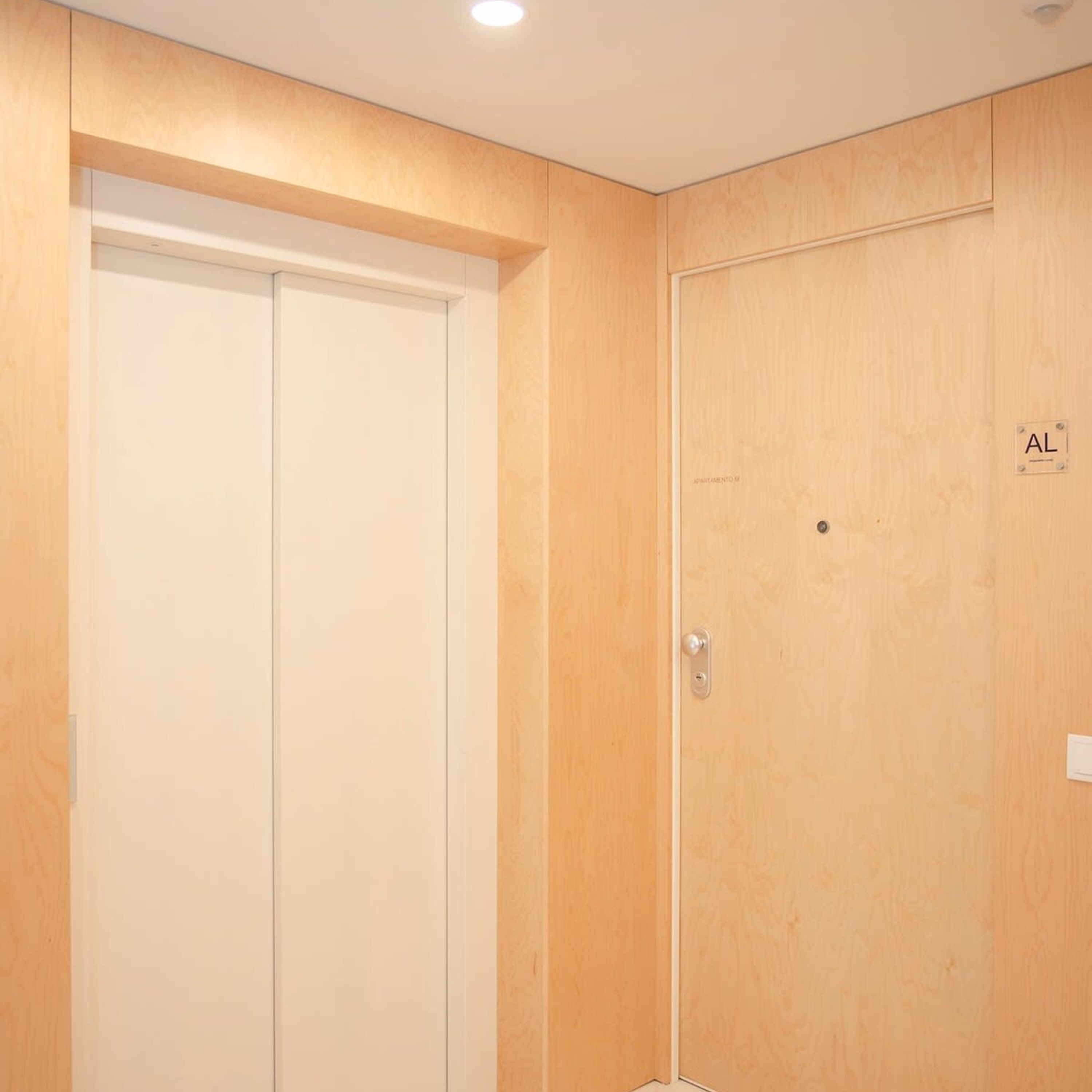 A hotel room with a wooden door, a visible "AL" sign, and a light switch on the wall.