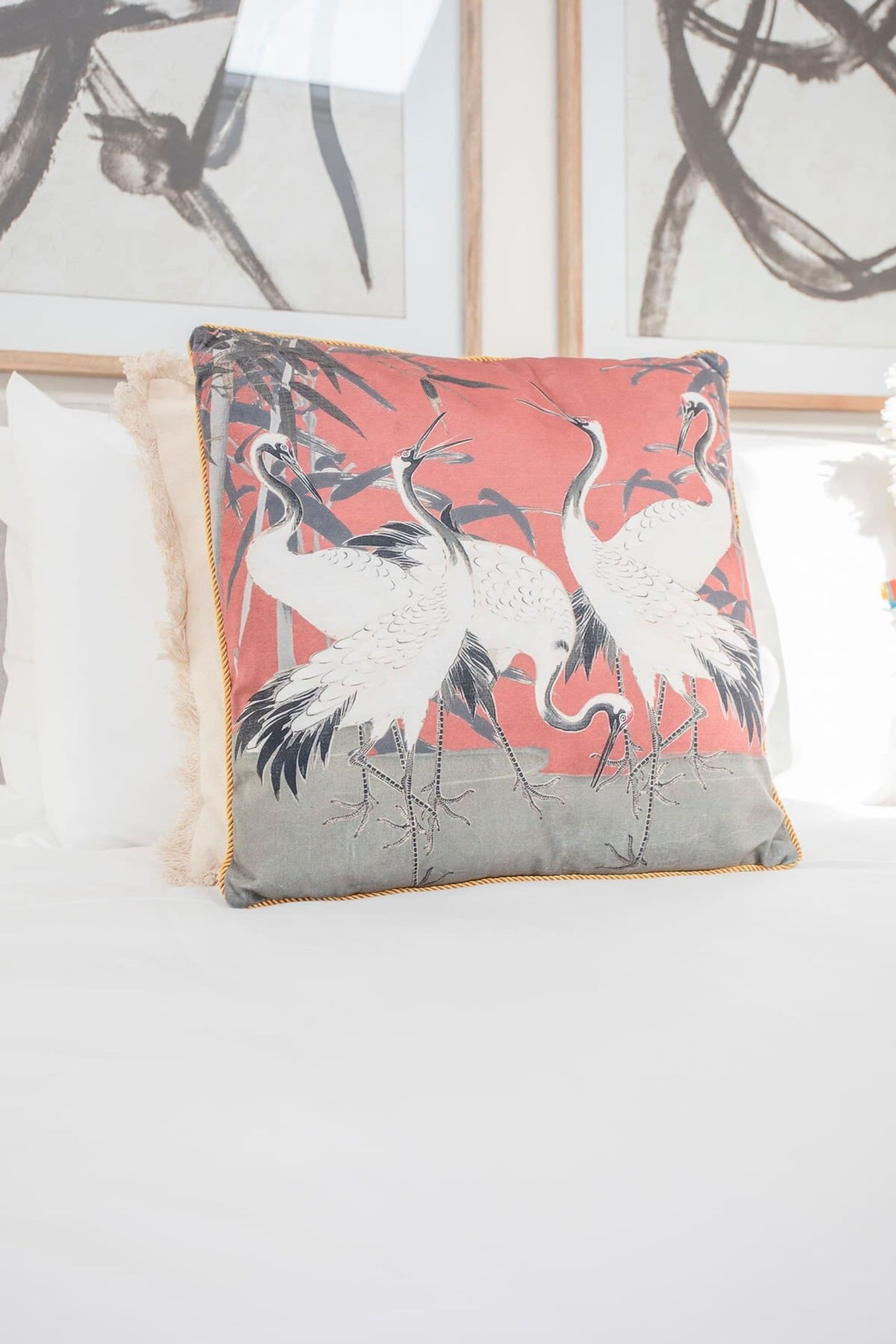 A pillow with a crane design on a white bed.
