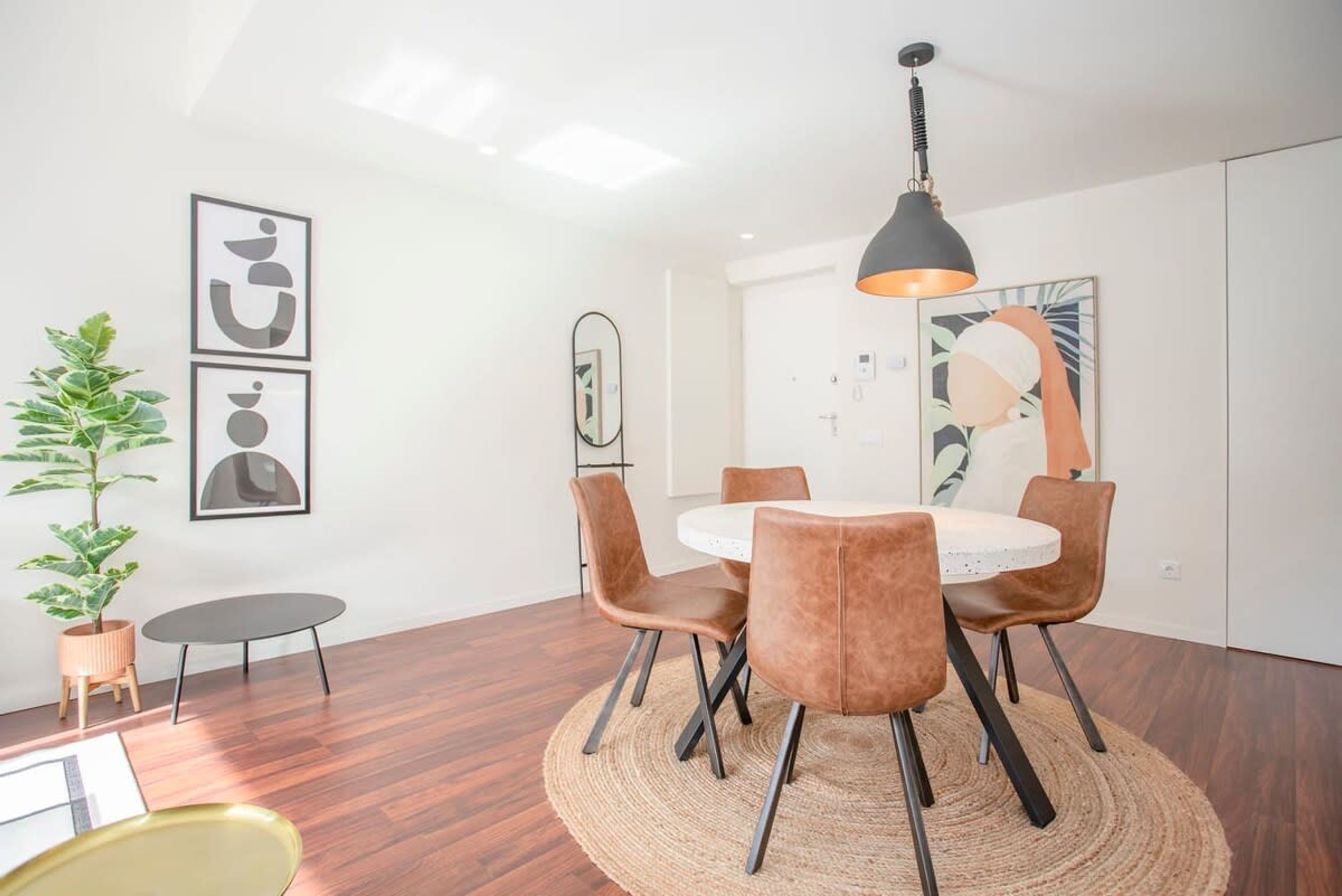 A dining area with a round table, six chairs, a woven rug, and a pendant light.