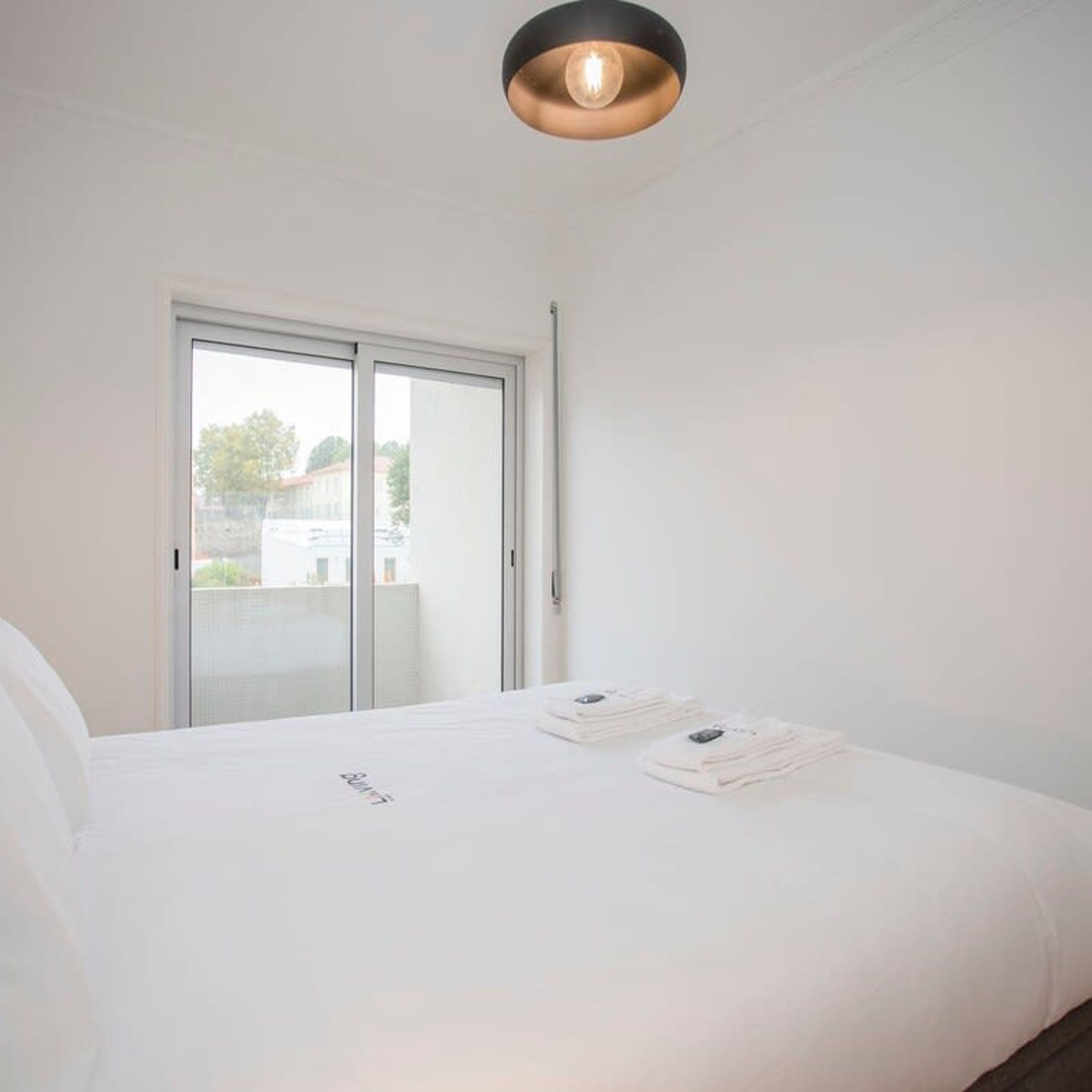 Une chambre à coucher avec un lit, une porte-fenêtre coulissante et un luminaire au plafond.