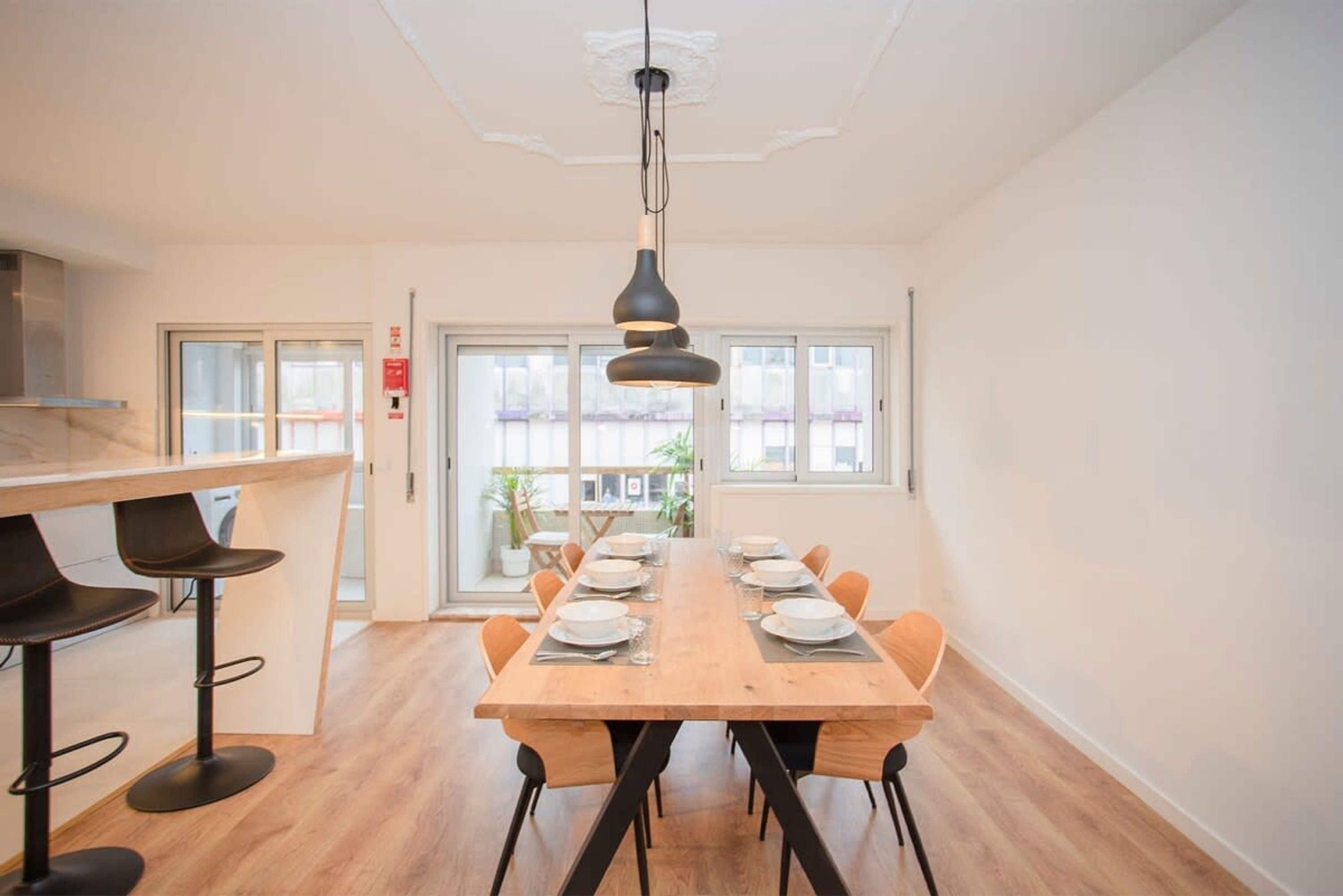 A modern dining area with a long wooden table set for six, surrounded by black chairs.