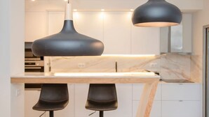 Eine moderne Küche mit Marmorarbeitsplatte, zwei Pendelleuchten und einer Bar mit Barhocker.