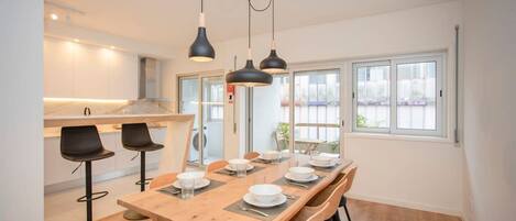 Un comedor moderno con una mesa de madera dispuesta para seis comensales, taburetes negros y lámparas colgantes.