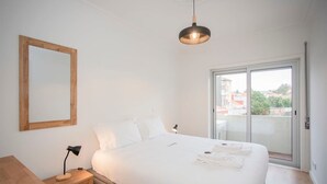Ein Schlafzimmer mit Bett, Schreibtisch, Nachttisch, Spiegel und einer Glastür zum Außenbereich.