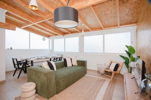 A spacious living area with a green sofa, wooden flooring, large windows, and a dining table set for four. - Liiiving in Porto - Downtown Quiet House (Porto)
