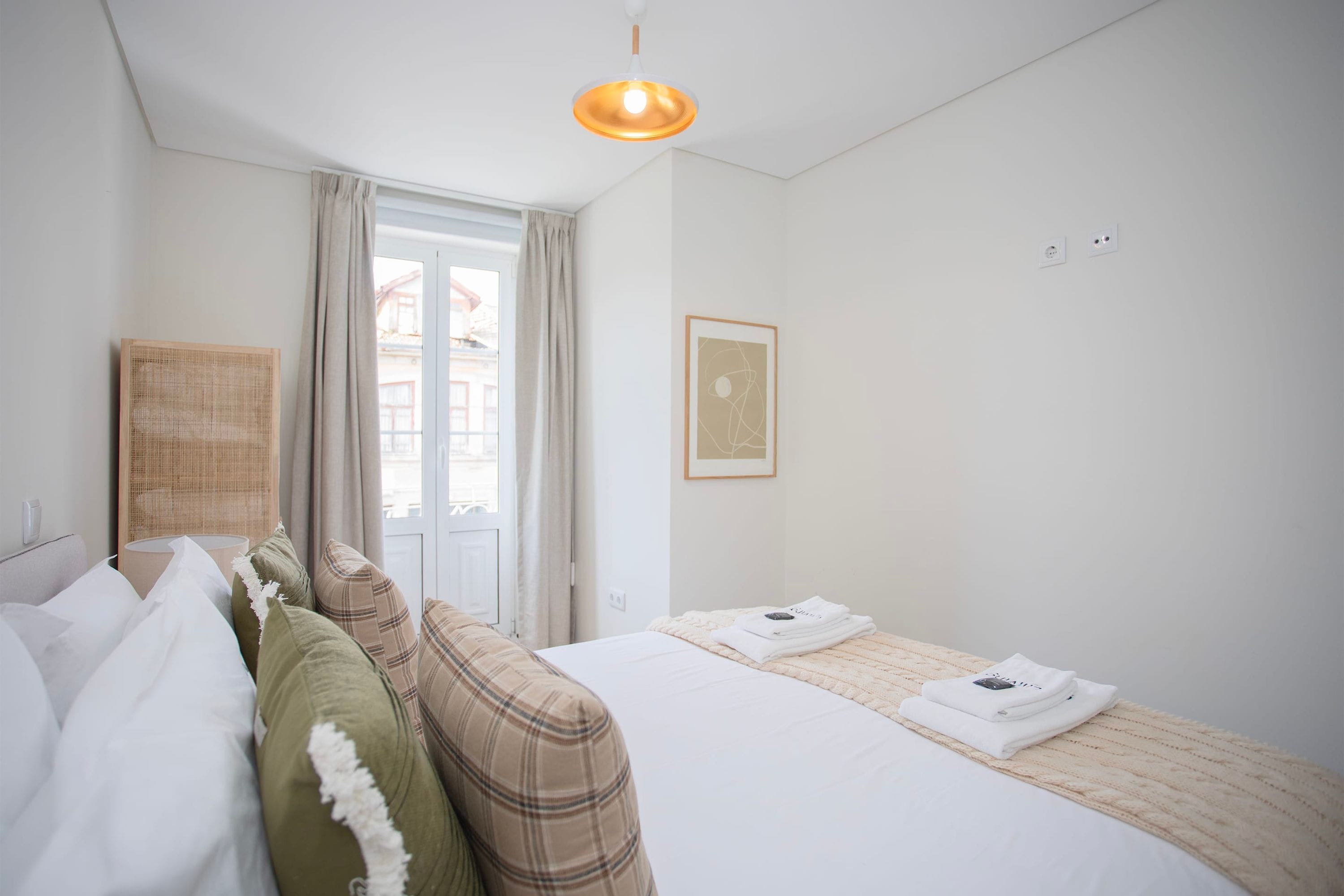 Ein Hotelzimmer mit Bett, einem Fenster mit Vorhängen, einer Wandlampe und einem gerahmten Bild.