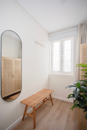 Una habitación con un banco de madera, un espejo grande, una ventana con cortinas y una planta en maceta.