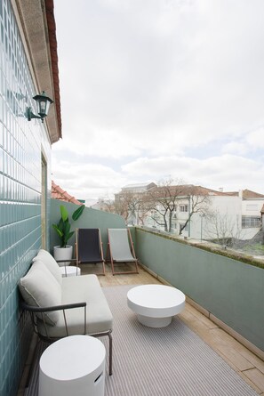 A balcony with a white sofa, two chairs, a small table, and a potted plant.